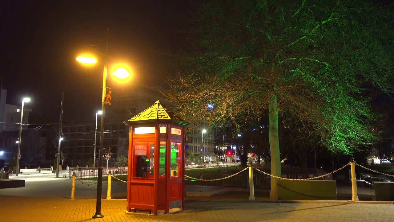 Old style phone box at night with changing colored lights on tree