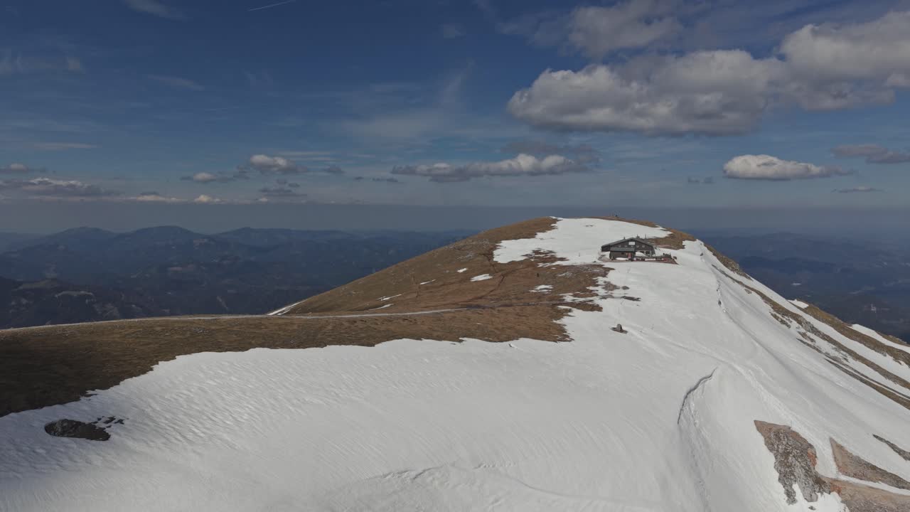 Vista aerea di una cresta montuosa aspra parzialmente coperta di neve, con una piccola baita alpina vicino alla cima.
