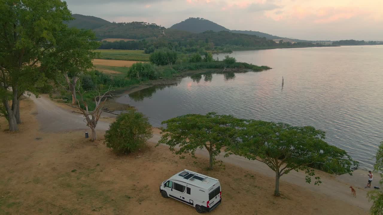 furgoneta blanca estacionada a orillas del lago trasimeno durante el amanecer en italia - toma aérea de drones