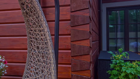 Shot-of-the-outside-of-a-wooden-house-with-a-swing-and-decorative-plants-visible-at-daytime