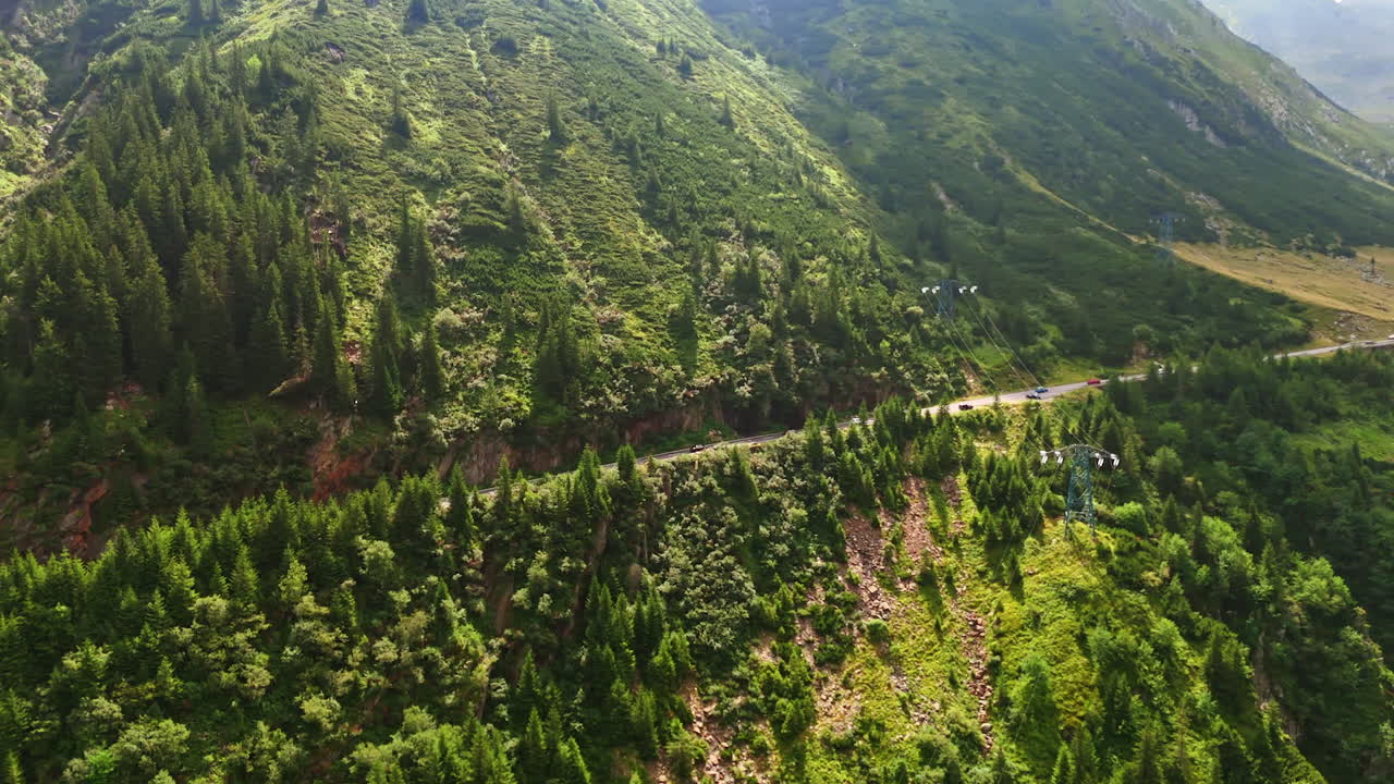 Huge green rocks covered with grass and pine trees. A highway passes the slope of the mountain. Romania wilderness