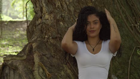 cerca de una joven y sexy modelo hispana jugando con su cabello parada frente a un gran árbol