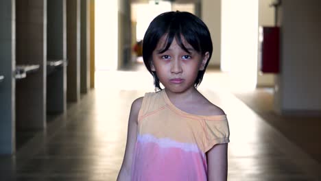 Portrait-of-a-young-Southeast-Asian-boy-alone-scared-looking-into-camera-in-an-abandoned-mall-hallway-with-light-and-shadow-in-the-background