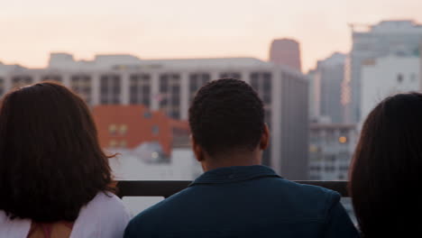 Rückansicht-Von-Freunden,-Die-Sich-Auf-Der-Dachterrasse-Mit-Blick-Auf-Die-Skyline-Der-Stadt-Versammelt-Haben