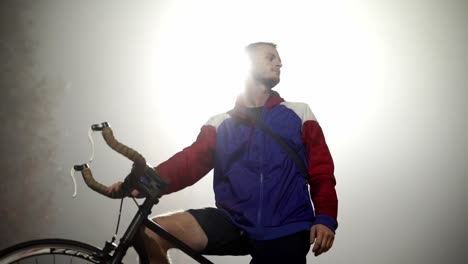 hombre atlético en bicicleta, retroiluminado por la luz de la calle en una noche nublada en cámara lenta