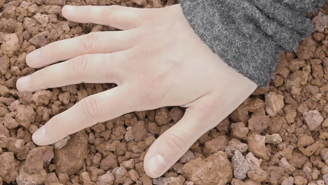 Close-up of a woman's hand sensually touching volcanic gravel
