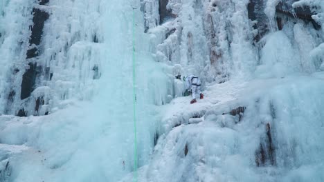 mountaineer ice climber climbing massive frozen icy cliff - wide angle