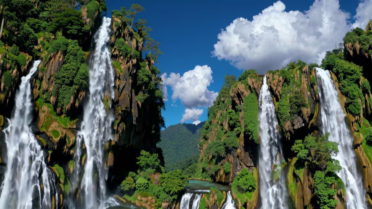 Aerial video captures majestic waterfalls cascading down lush cliffs under a clear blue sky
