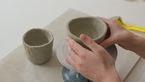 colocando taza de arcilla en una rueda giratoria, preparándose para la artesanía en un estudio encantador