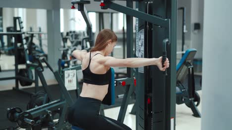 a woman with a sporty figure is sitting and doing an exercise to strengthen the back muscles in the gym. blurred background