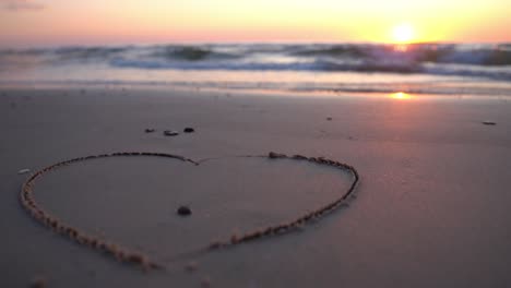 heart symbol drawn on sand against a backdrop of sunset over the sea