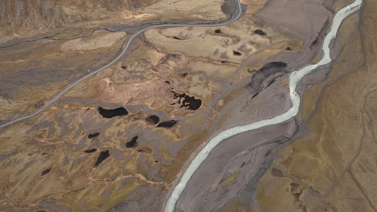 아이슬란드 남부의 황량하고 거친 지형을 가로질러 흐르는 빙하 강의 드론, 눈에 띄는 도로와 풍경에 어져있는 연못