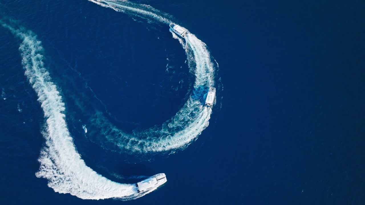 Top down aerial shows white boat creating circular wake on glassy blue sea