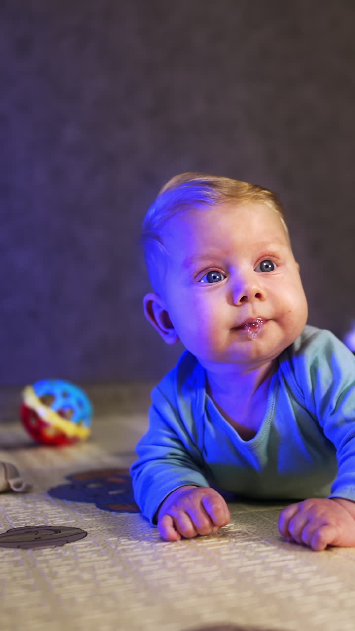 Little infant baby with fair hair lies on his belly. Peaceful baby boy looking up with interest. Vertical video