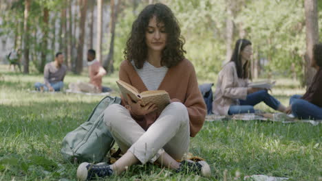 young woman reading in a park with friends