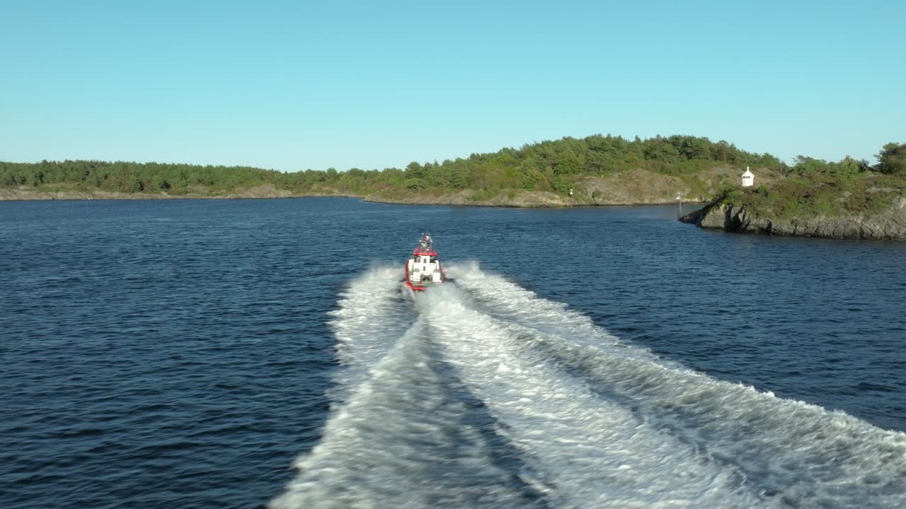 A fast boat navigates the tranquil waters, leaving a wake behind as it approaches a rocky coastline. Lush greenery adorns the shore, with a lighthouse visible in the distance