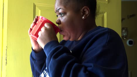 african american woman in front of yellow door drinking coffee in a red mug