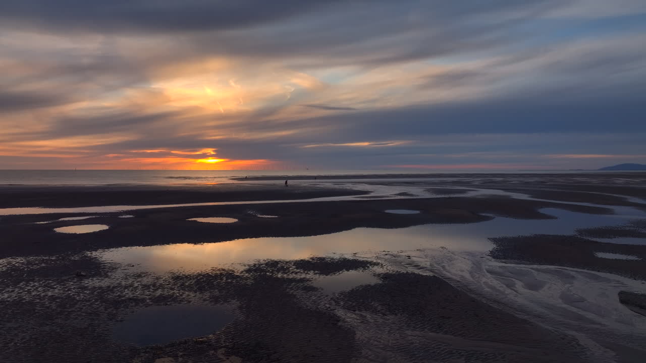 Tidal pool reflections and fishermen with setting sun. Lateral flight. Fleetwood, Lancashire, UK