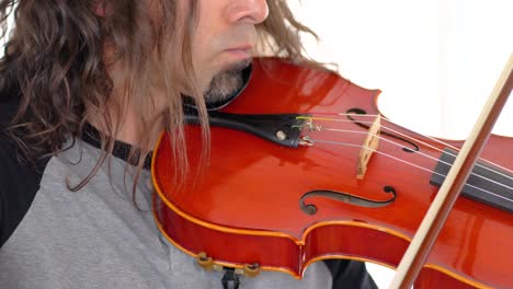 close up of ethnic musician in grey shirt with long hair and goatee playing music on red viola