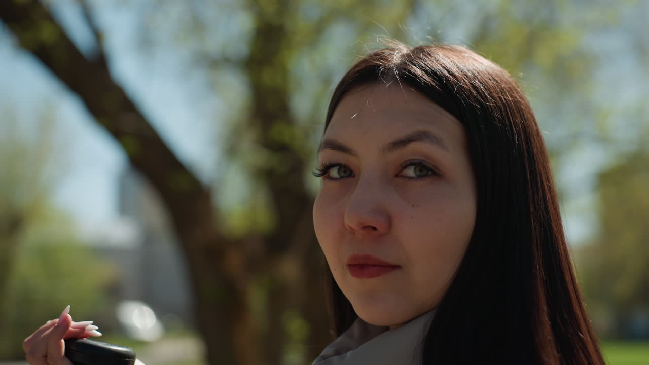 햇빛 아래에서 자연스러운 아름다움을 돋보이게 하는 사람, 공원에서 한 여성이 야외에서 간단하게 화장을 수정하는 장면, 햇빛과 공원 환경 속에서 휴대용 거울을 보며 화장을 고치는 모습