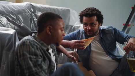 los chicos afroamericanos positivos disfrutan de cerveza y pizza cerca del sofá