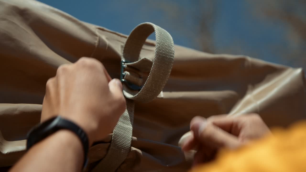 Close-up shot of a tourist's hands as he loosens the straps of his canvas rooftop tent.