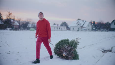 Happy-man-pulling-sled-with-Christmas-tree-on-snow-covered-landscape