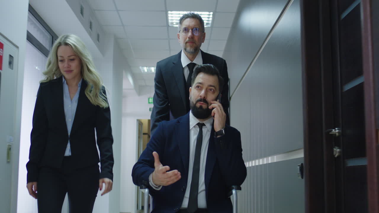 Wheelchair Manager Phoning in Office Corridor. Medium shot of disabled manager phoning while colleague pushing her wheelchair in office corridor
