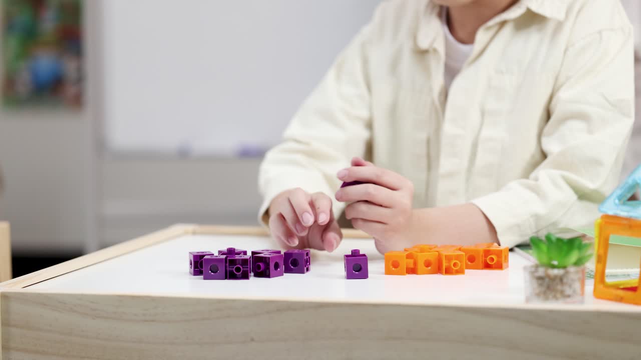 Un bambino esercita le capacità motorie fini ordinando blocchi viola e arancioni a un tavolo