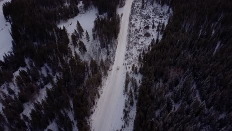 White-truck-driving-on-snowy-winter-road-in-Canadian-Prairies-surrounded-by-forest