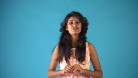 A-young-Indian-girl-in-orange-frock-giving-'wow'-expression-smiling-at-the-camera-standing-in-an-isolated-blue-background