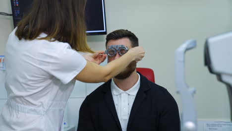 man examining his eyesight in modern clinic. doctor ophhalmologist putting on trial frame with lenses on a patient eyes. slow motion.