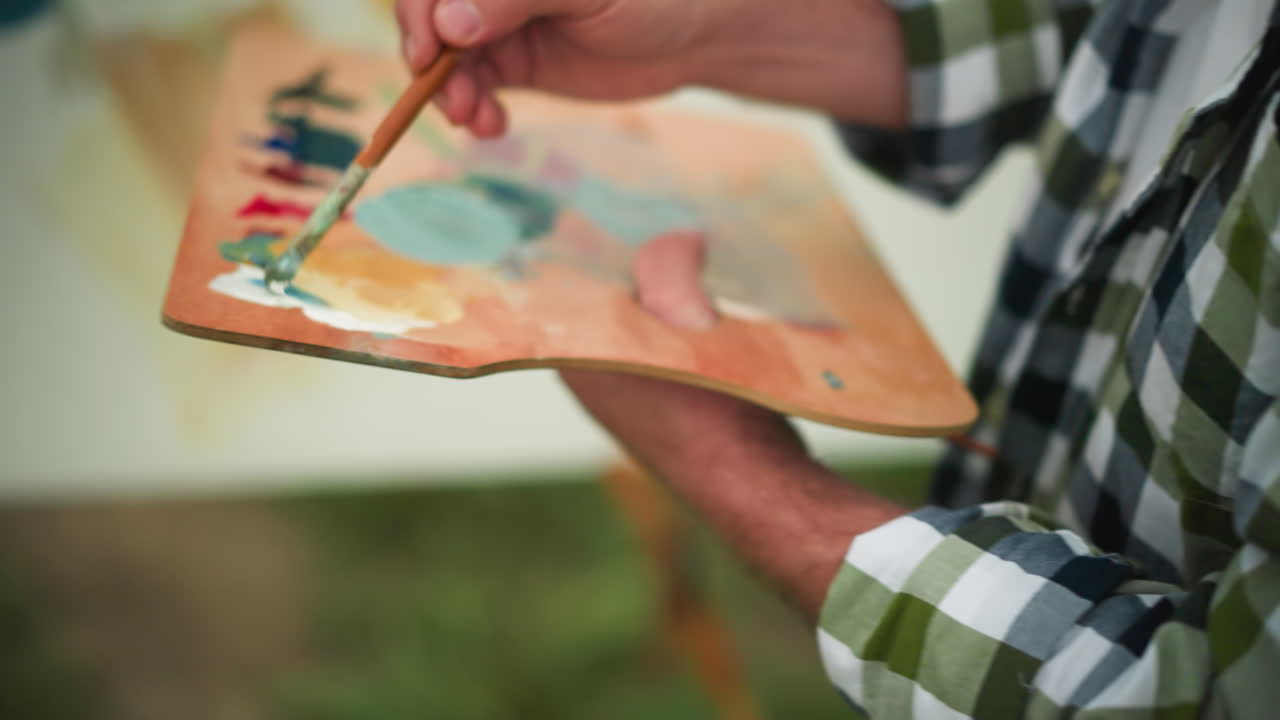 un pintor sostiene delicadamente una paleta de madera llena de pintura vibrante mientras aplican los toques finales a su obra de arte. centrándose en la mano y el pincel en acción