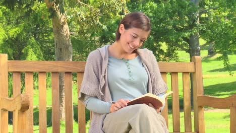mujer joven leyendo un libro en un banco