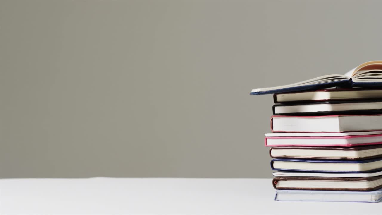 Close up of open book on stack of books with copy space on grey background, in slow motion