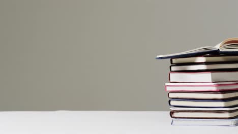 close up of open book on stack of books with copy space on grey background, in slow motion
