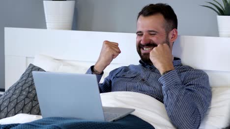 reacción de éxito por hombre feliz usando portátil en la cama