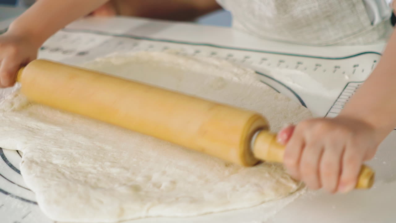 little girl rolls dough with wooden pin at table in kitchen