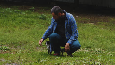 Middle-aged-man-playing-with-black-and-white-tabby-cat-in-garden-grass