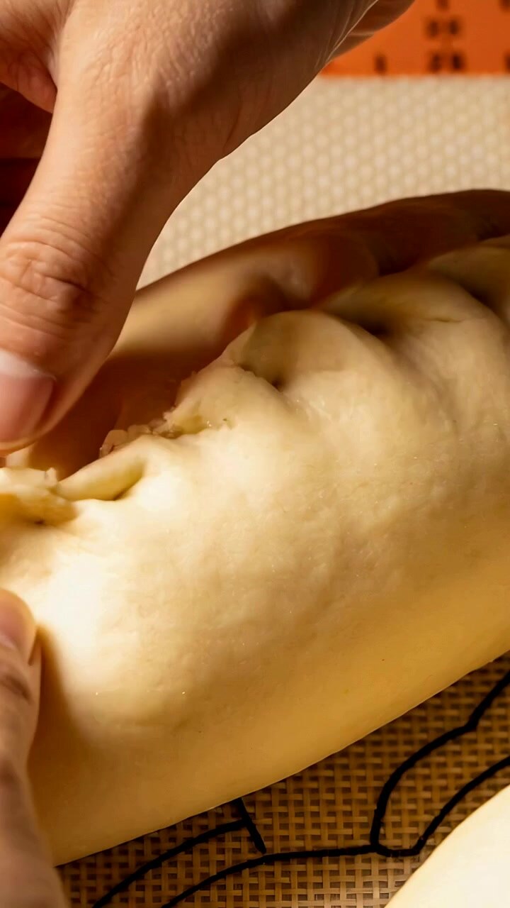 Vertical video: First pinch starting hands sealing seam on dough roll on silicone mat, second piece