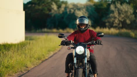 A-man-in-a-red-sweater-and-a-motorcycle-helmet-effectively-turns-on-the-road-on-a-motorcycle-in-sunny-weather.-Motorcycle-riding-as-a-hobby