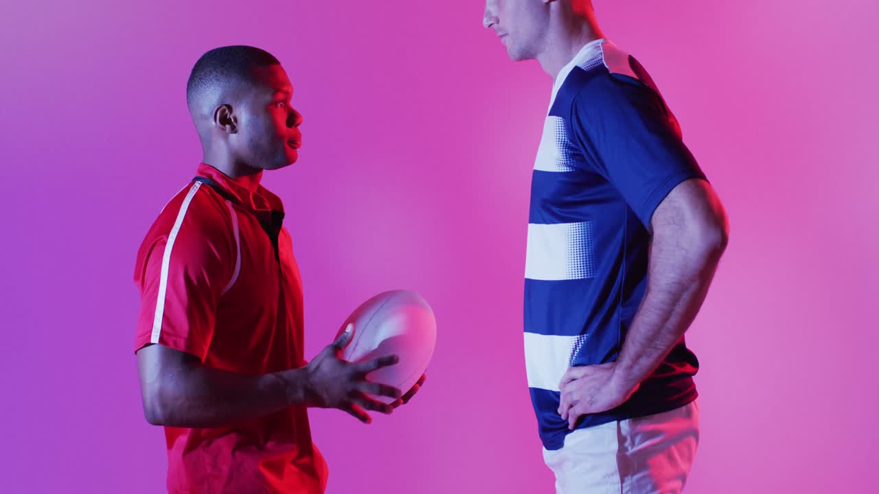 Diverse male rugby players with rugby ball over pink lighting