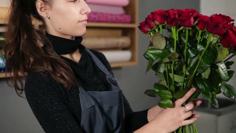 Young-attractive-female-florist-arranging-bouquet-of-beautiful-red-roses-at-flower-shot.-Slow-Motion-shot