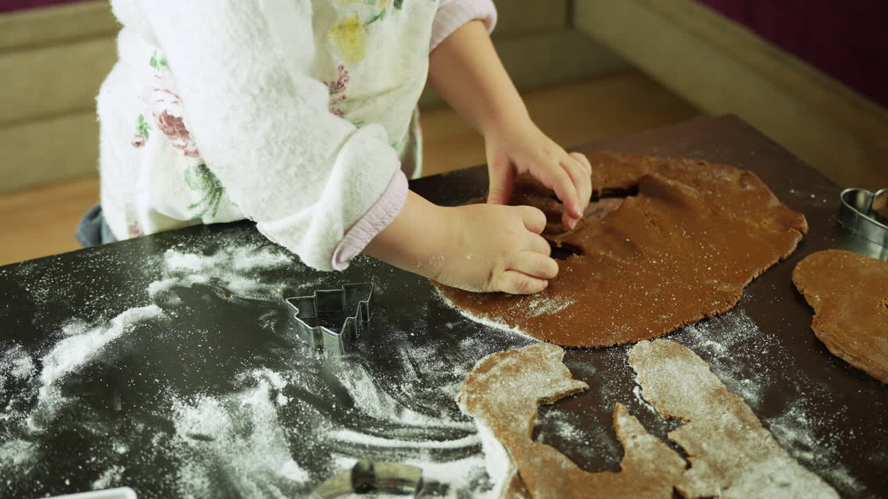 Kid preparing christmas cookies using cookie cutters and dough on a kitchen table at home in a messy setting