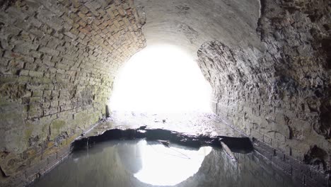 old brick abandoned semicircular drainage tunnel that goes outside, timelapse, with overexposed white free space.