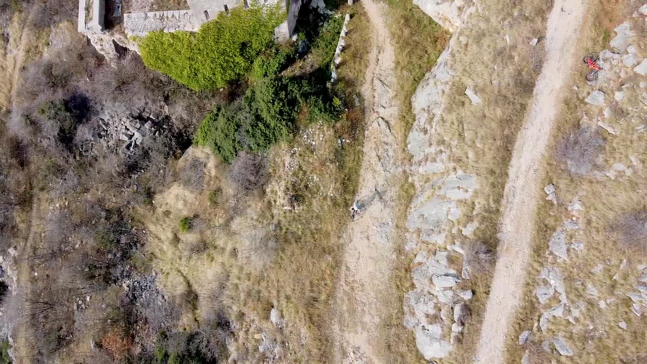 disparo de drones de un ciclista de montaña cabalgando sobre un camino de grava lejos de un castillo en ruinas
