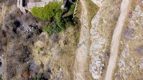 Drohnenaufnahme-Eines-Mountainbikers,-Der-Auf-Einer-Schotterstraße-Weg-Von-Einer-Burgruine-Fährt