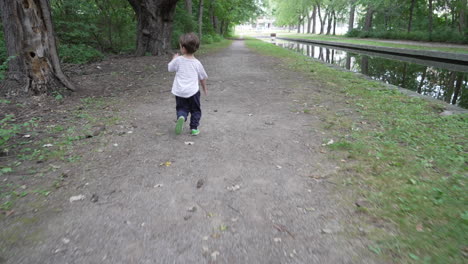 child running in outdoor garden. kid skipping and walking through the forest and walking beside duck pond. camera moving forwards and following a happy young boy.