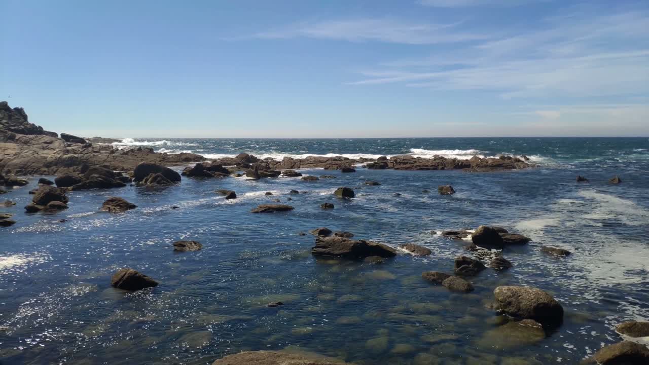 marea baja con reflejos del sol y olas rompiendo contra las rocas del acantilado en un día soleado sin nubes, disparando hacia la izquierda, islas cíes, pontevedra, galicia, españa
