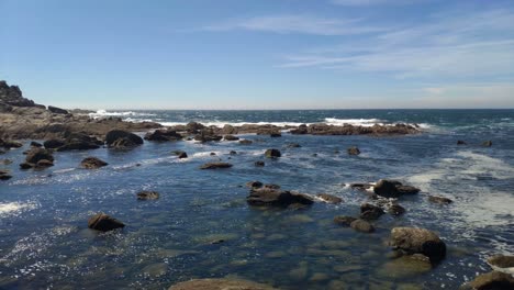 Marea-Baja-Con-Reflejos-Del-Sol-Y-Olas-Rompiendo-Contra-Las-Rocas-Del-Acantilado-En-Un-Día-Soleado-Sin-Nubes,-Disparando-Hacia-La-Izquierda,-Islas-Cíes,-Pontevedra,-Galicia,-España